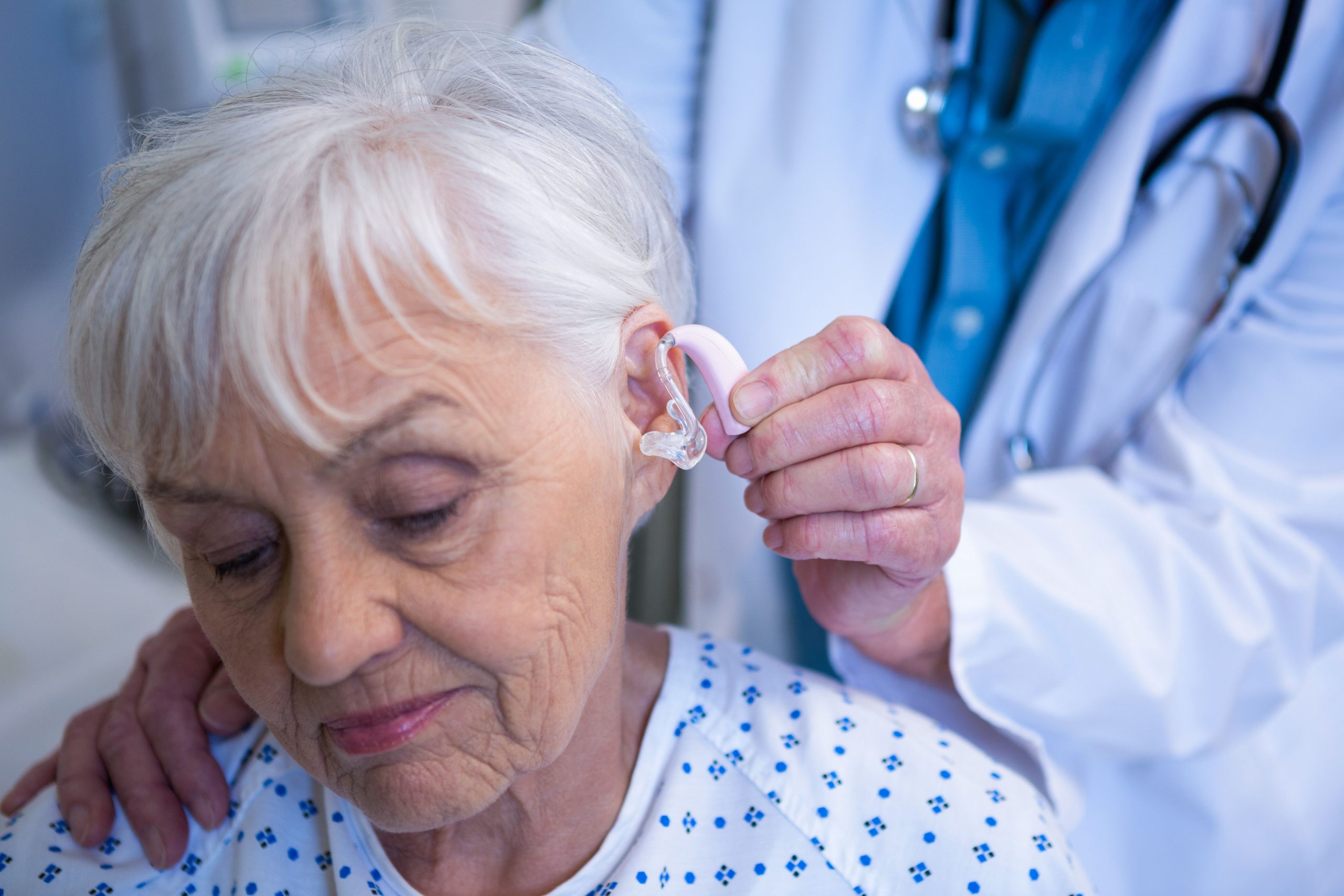 Doctor inserting hearing aid in senior patient ear Photo ...